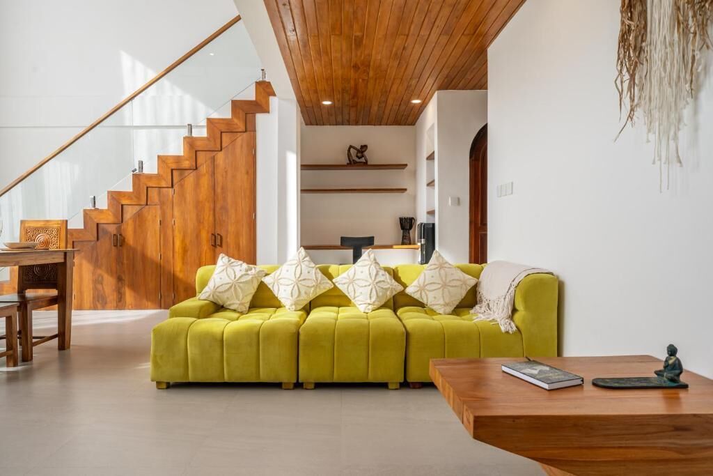 A modern living room with a wooden staircase, a green sofa, and a wooden coffee table.