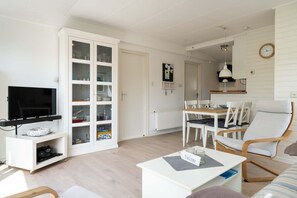 Ein Wohnzimmer mit Fernseher, weißen Schränken, einem Esstisch mit Stühlen und einer Couch.