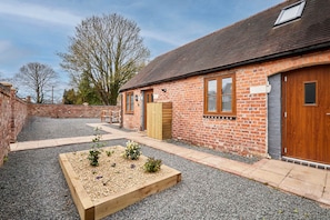 A brick building with a wooden door, a small garden area with raised beds, and a gravel driveway. - Host Stay Beagle Barn (Shrewsbury)