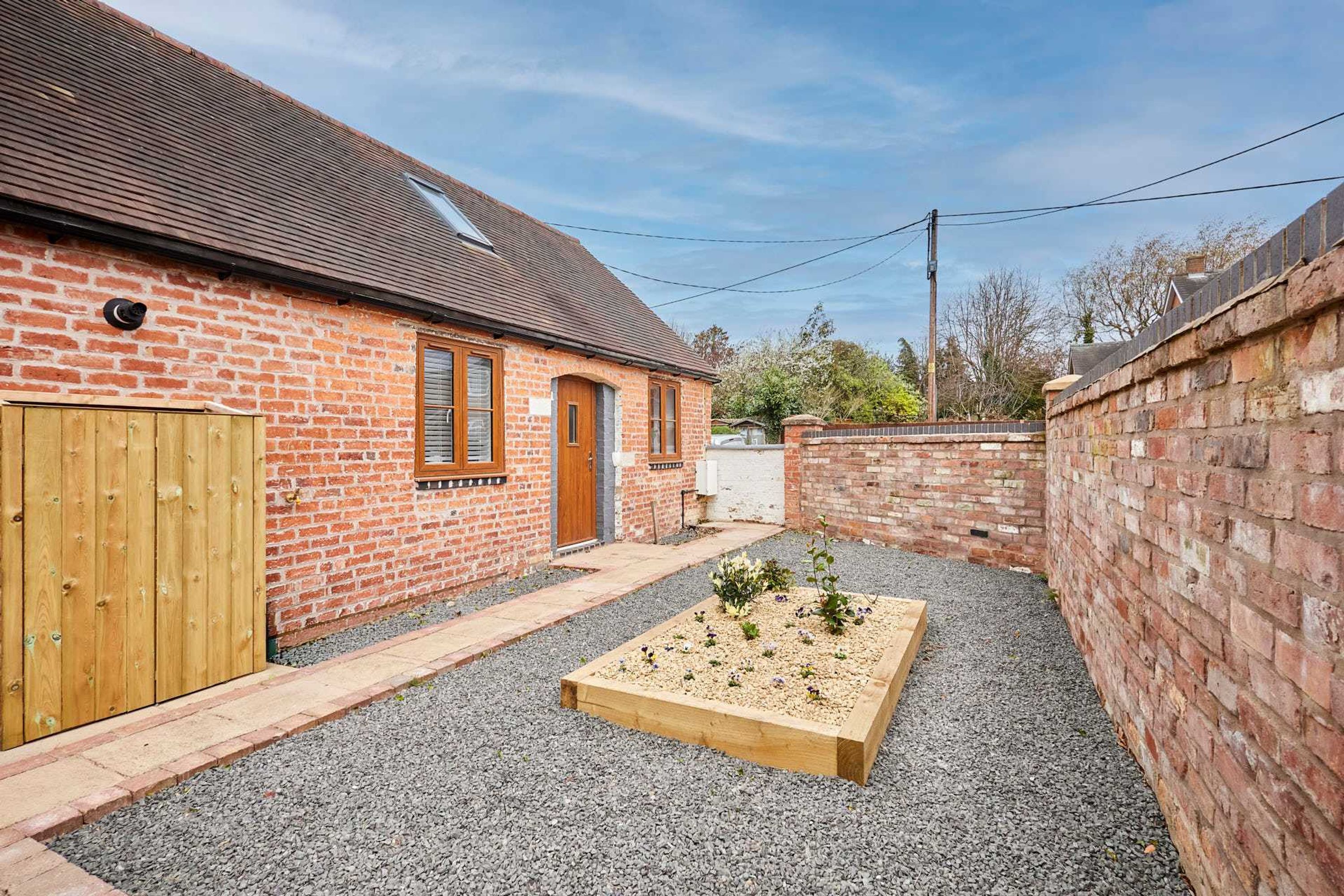 A brick house with a wooden door, a small garden bed, and a gravel driveway.