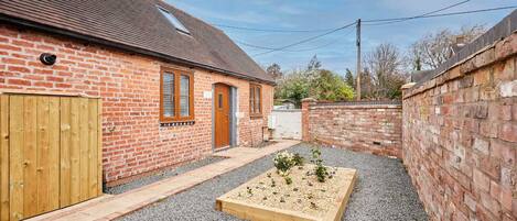 A brick house with a wooden door, a small garden bed, and a gravel driveway.