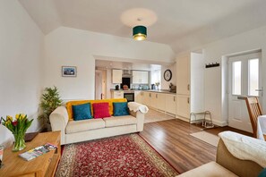 Uma sala de estar com sofá, mesa de centro, tapete e um espaço de jantar com cadeira e mesa.