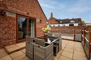 A patio with wicker furniture, a glass table, and a brick building with a sliding glass door. - Host Stay Beagle Barn (Shrewsbury)