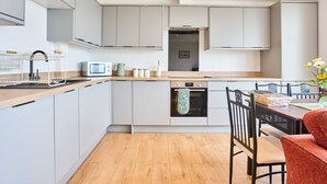 Uma cozinha moderna com armários cinzentos, bancada de madeira, micro-ondas, chaleira e área de refeições com mesa e cadeiras.