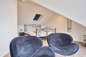 A bedroom with a skylight, a bed with floral bedding, and two dark chairs. - Host Stay 2b Hamilton Road (Felixstowe)