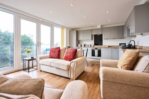 A modern living room with a sofa, a coffee table, and a kitchen in the background. - Host Stay 2a Hamilton Road (Felixstowe)