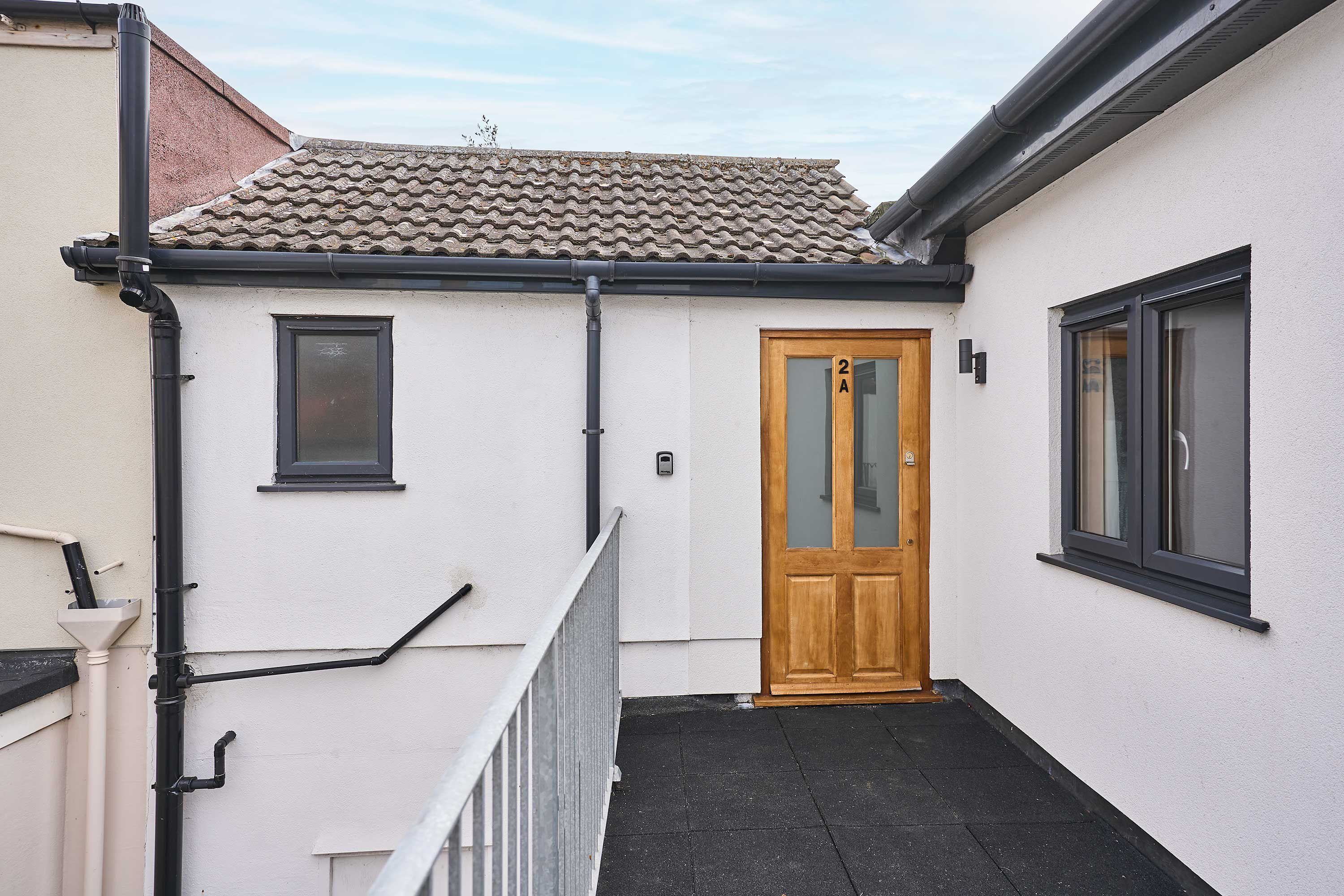 A narrow corridor with a wooden door, a window, and a black tiled roof.