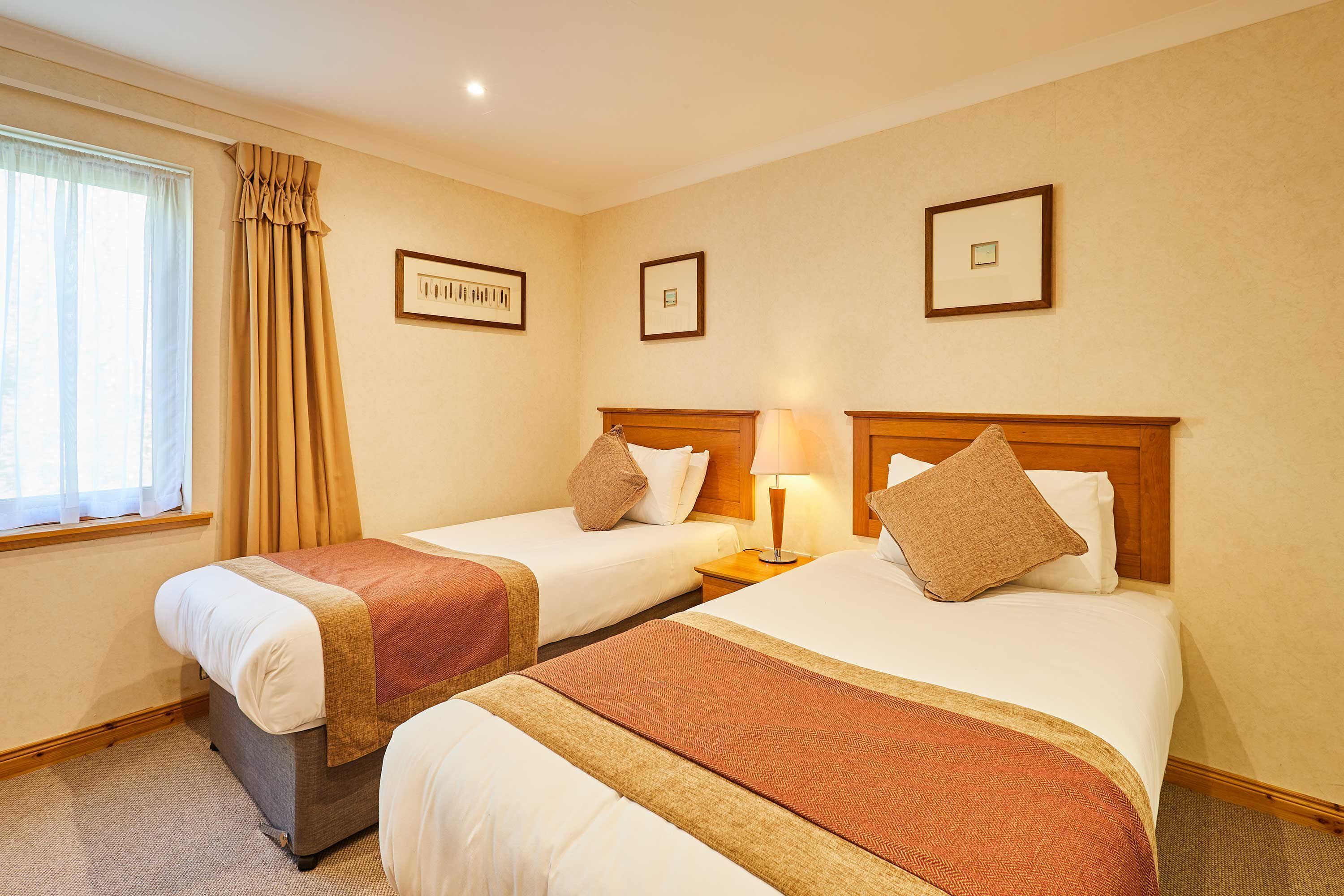 A hotel room with two beds, a window with curtains, and framed pictures on the wall.