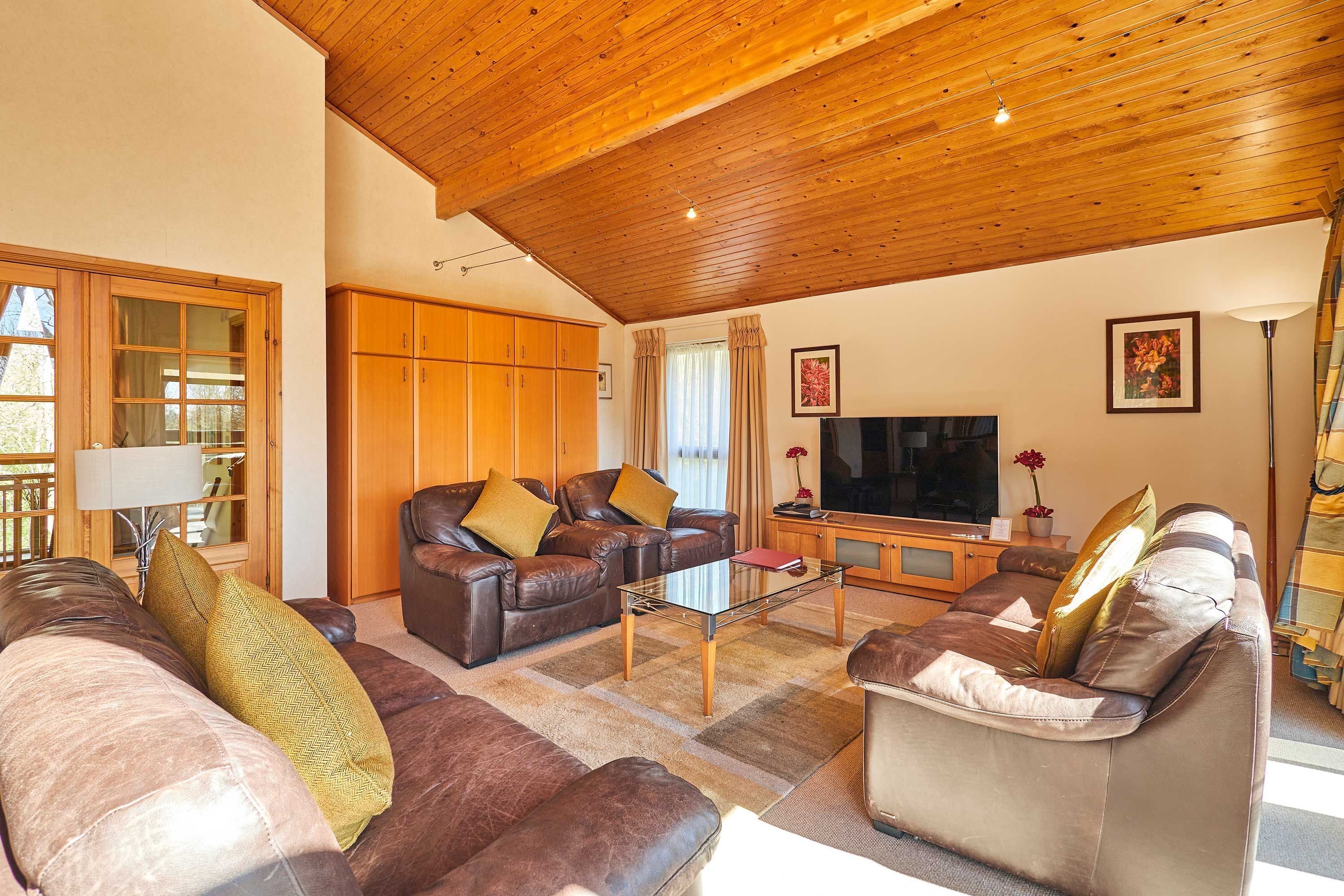 A living room with leather sofas, a glass coffee table, wooden ceiling, and a television.