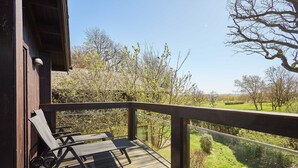 Een houten terras met een tafel en stoelen, met uitzicht op een grasveld met bomen.