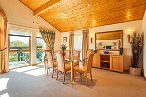 A dining area with a glass table, wooden chairs, a wooden ceiling, and a view through large windows. - Host Stay Lodge 32 (Grantham)