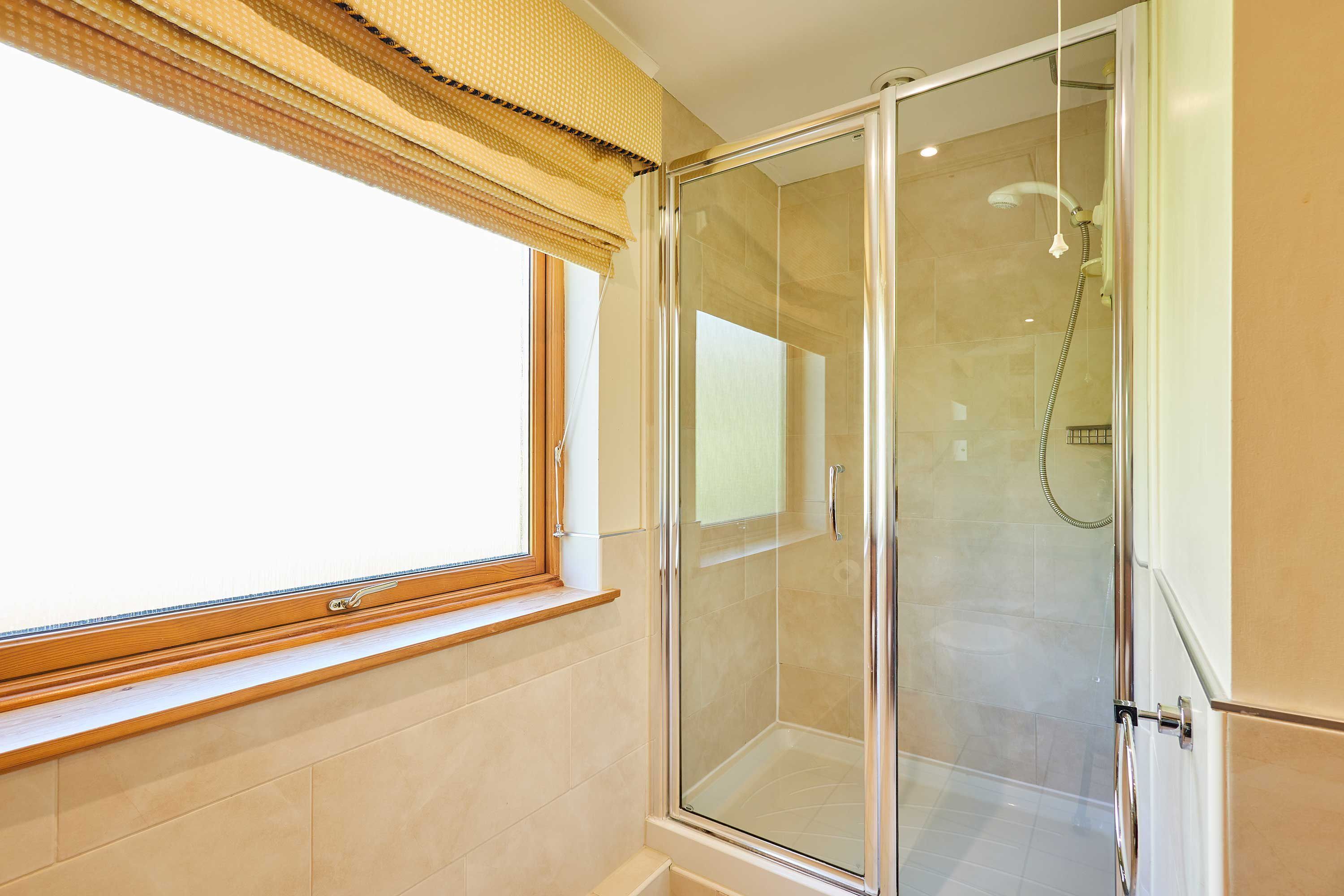 Un baño con cabina de ducha de vidrio, una ventana con marco de madera y suelo de baldosas.