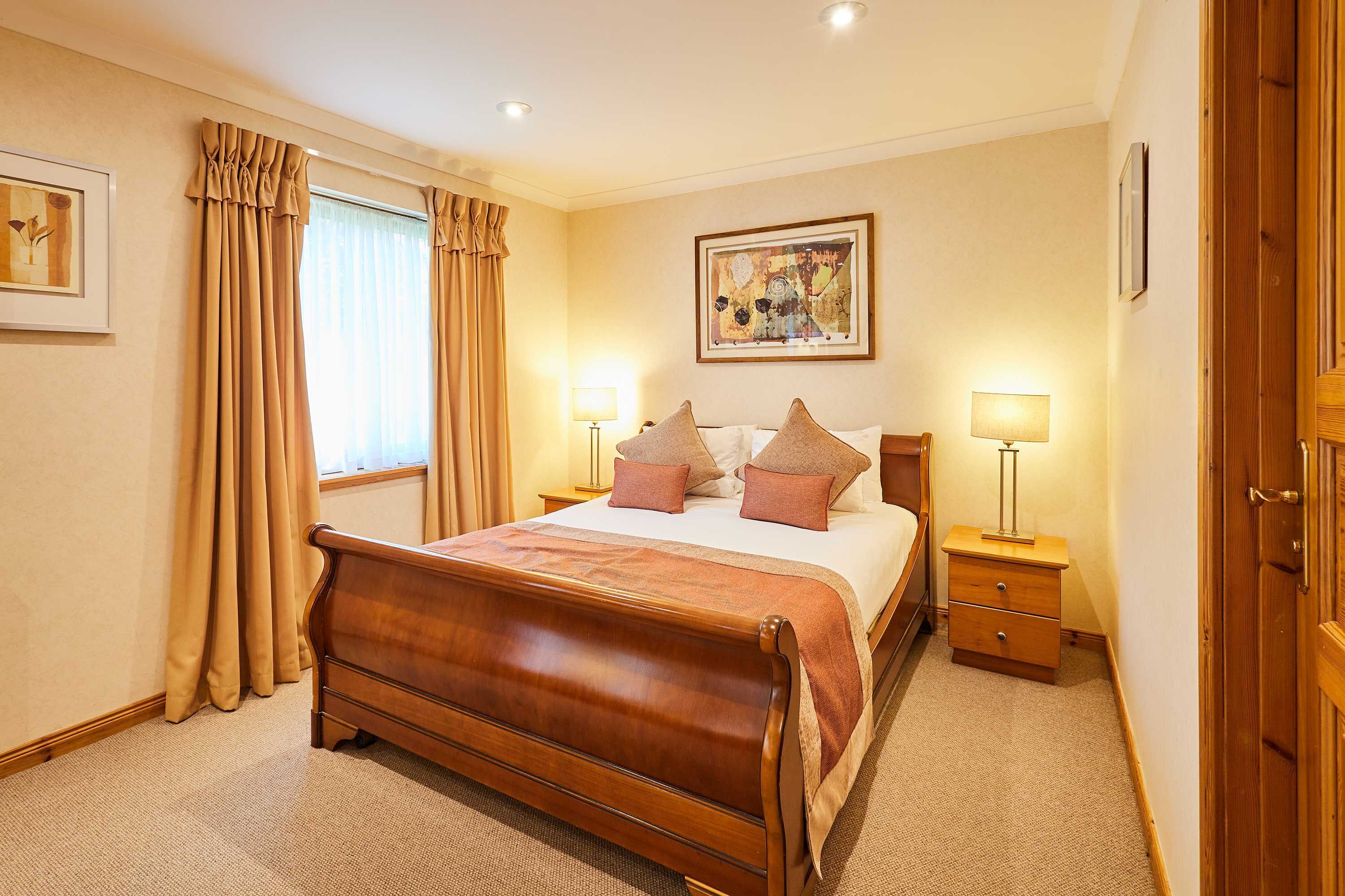 Hotelkamer met een houten bed, twee nachtkastjes met lampen, een lijst aan de muur en een raam met gordijnen.