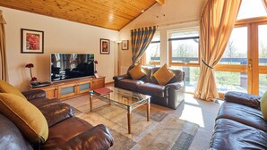 Een woonkamer met een houten plafond, leren banken, een glazen salontafel en een televisie.