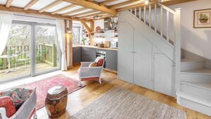 A spacious kitchen with wooden beams, a staircase, and a dining area with a red sofa and a patterned rug. - Host Stay Tree House (Lewes)