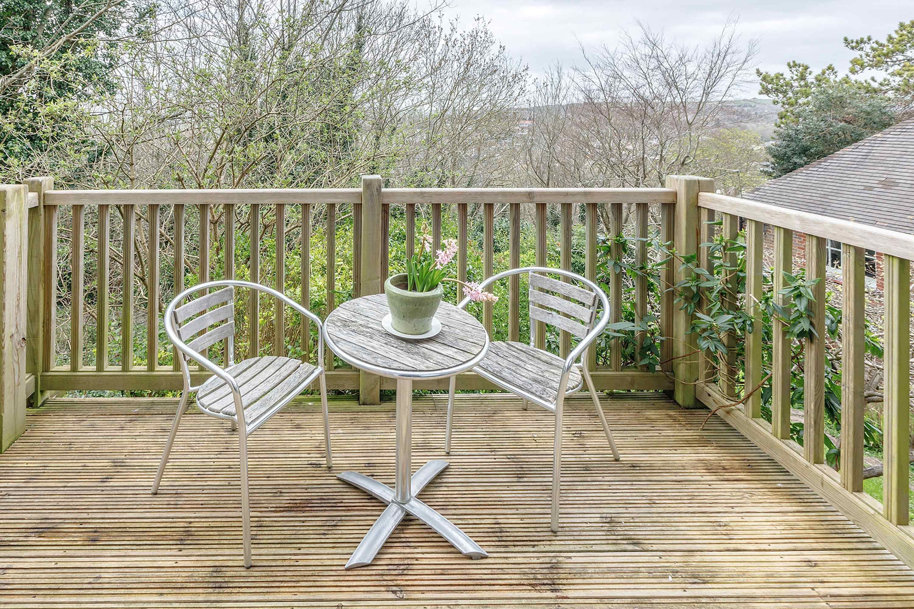A wooden deck with a metal table and two chairs, surrounded by a wooden railing.