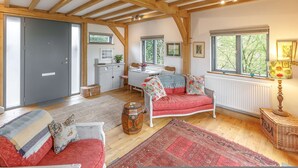 A cozy room with a wooden ceiling, a red sofa, a white table, and a window with a view of trees. - Host Stay Tree House (Lewes)