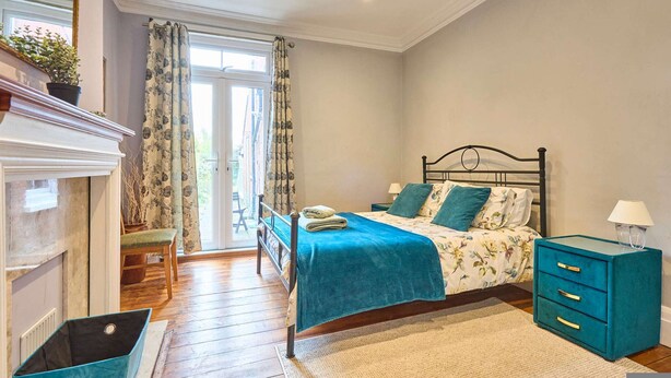 Een slaapkamer met een bed, nachtkastje, kaptafel, raam met gordijnen en een open haard.