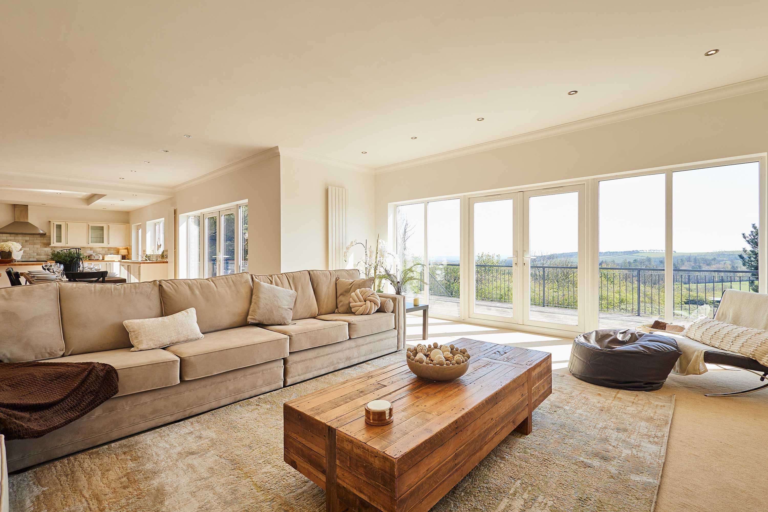 Ein geräumiges Wohnzimmer mit einer großen Couch, einem Holztisch und Blick ins Freie.