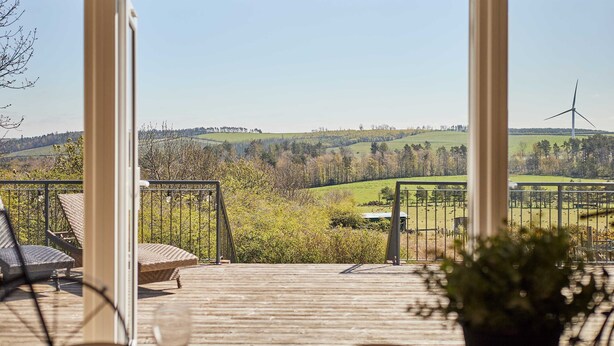 A wooden deck with a view of a rural landscape, including a wind turbine and rolling hills. - Host Stay Forest View Lodge (Durham)
