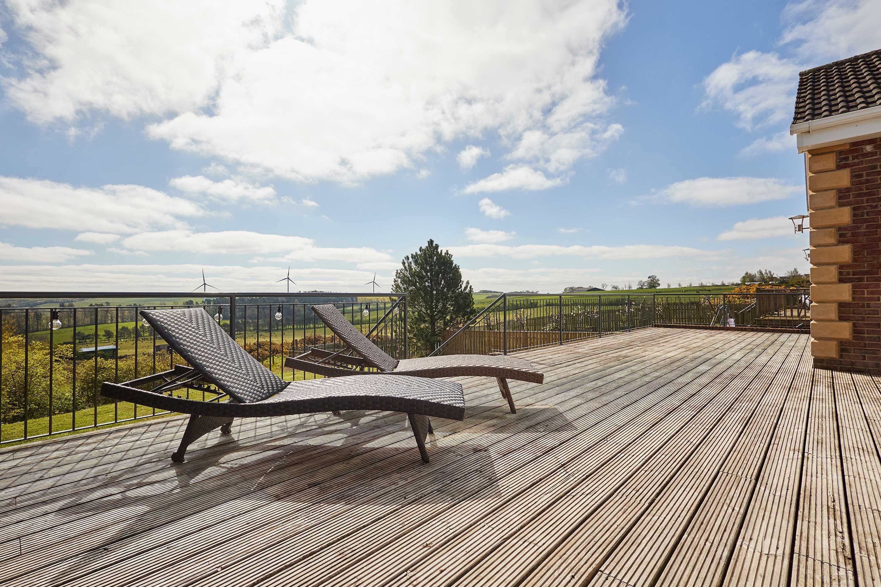 Une terrasse en bois avec des chaises longues et une vue sur des éoliennes et la verdure.