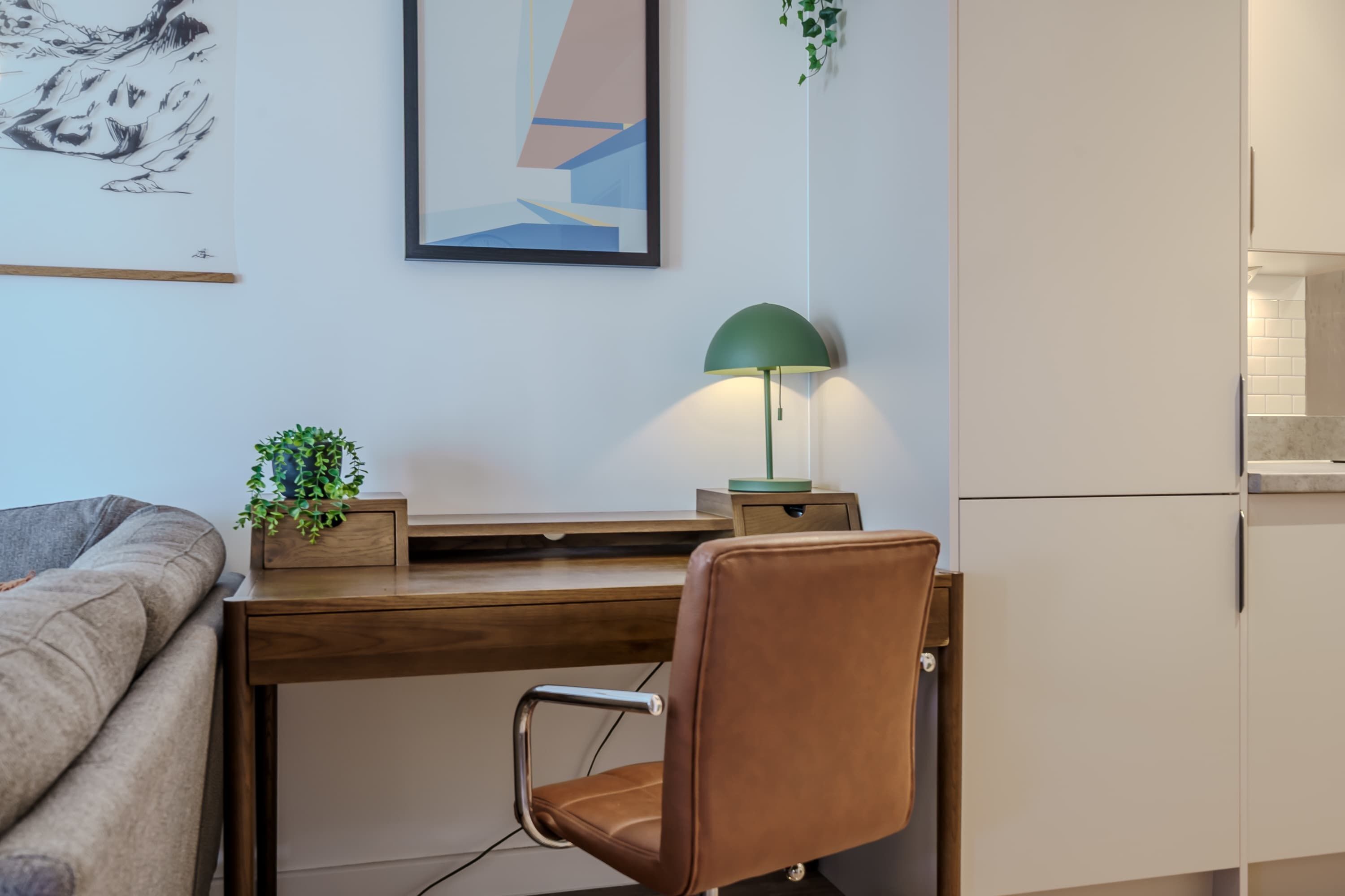 A modern workspace with a desk, chair, lamp, and a painting on the wall.