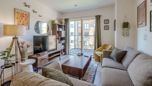 A living room with a sofa, coffee table, TV, bookshelf, and a balcony with a view of buildings. - Host Stay Austin House (Norwich)