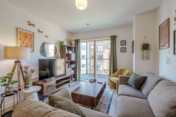 Un salon comprenant un canapé, une table basse, un téléviseur, une bibliothèque et un balcon offrant une vue sur les immebles.