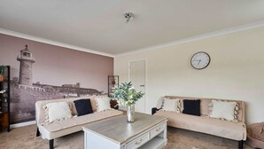 A living room with two sofas, a coffee table, a clock, and a lighthouse mural on the wall. - Host Stay Paylors View Cottage (Whitby)