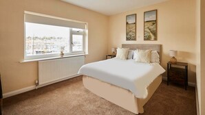 A bedroom with a large bed, a window with a view, and two wall-mounted paintings. - Host Stay Paylors View Cottage (Whitby)