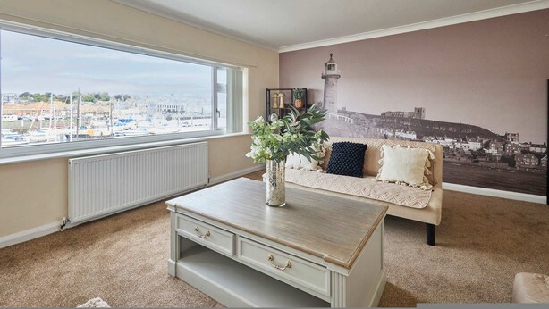 A room with a large window, a sofa, a coffee table, and a mural of a lighthouse. - Host Stay Paylors View Cottage (Whitby)