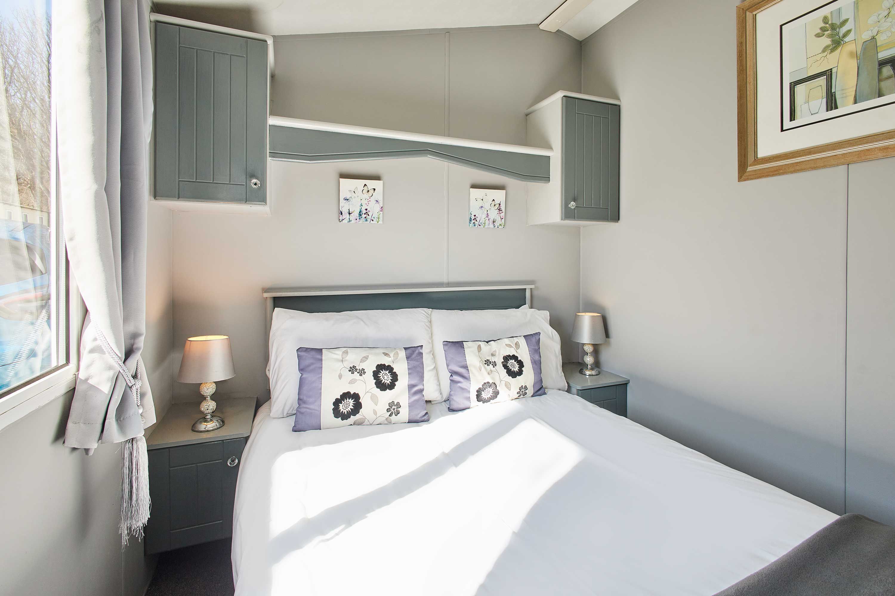 A neatly made bed with floral pillows, a bedside lamp, and a nightstand with a lamp.