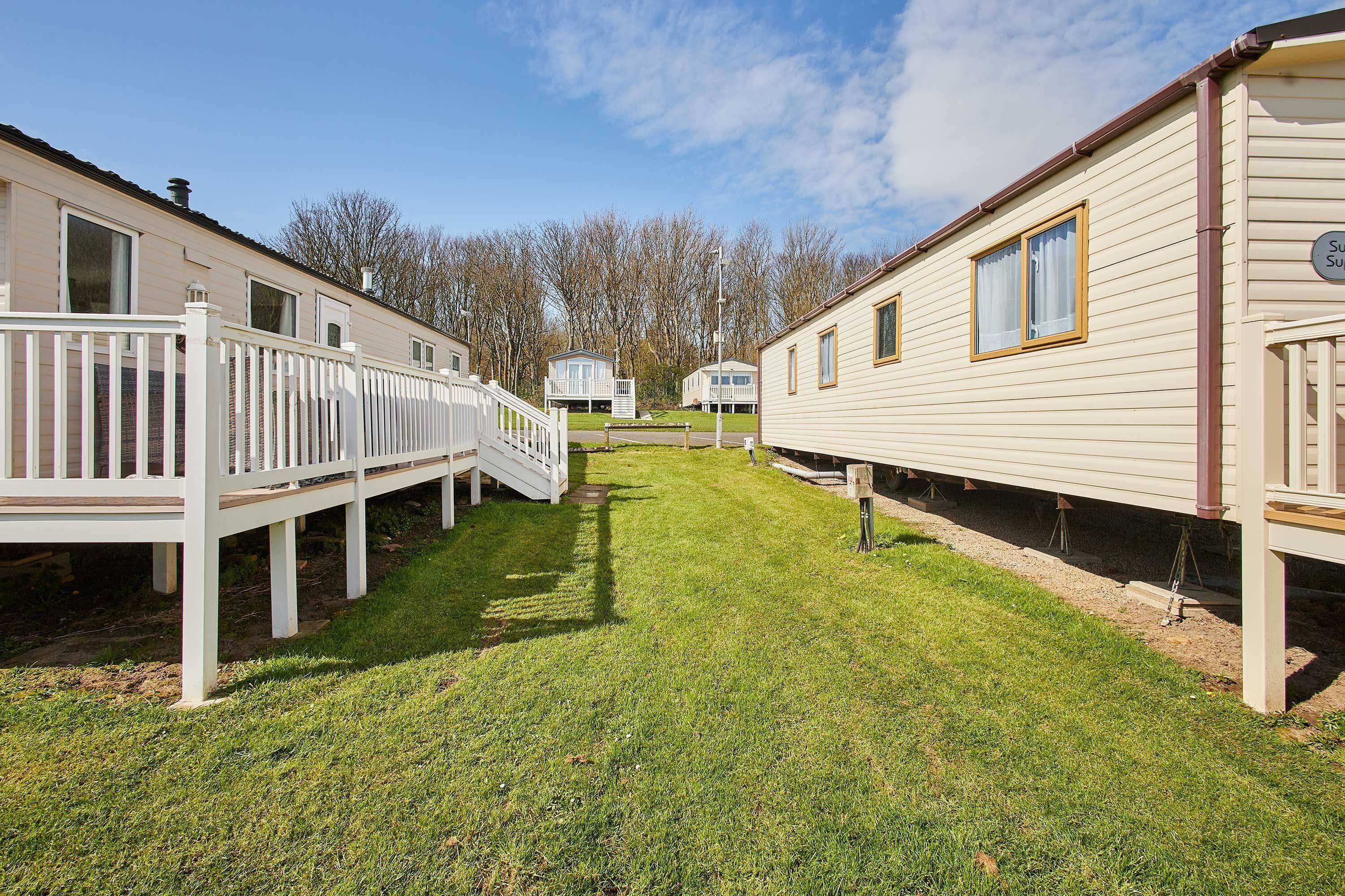 A row of mobile homes with white railings and a grassy yard.