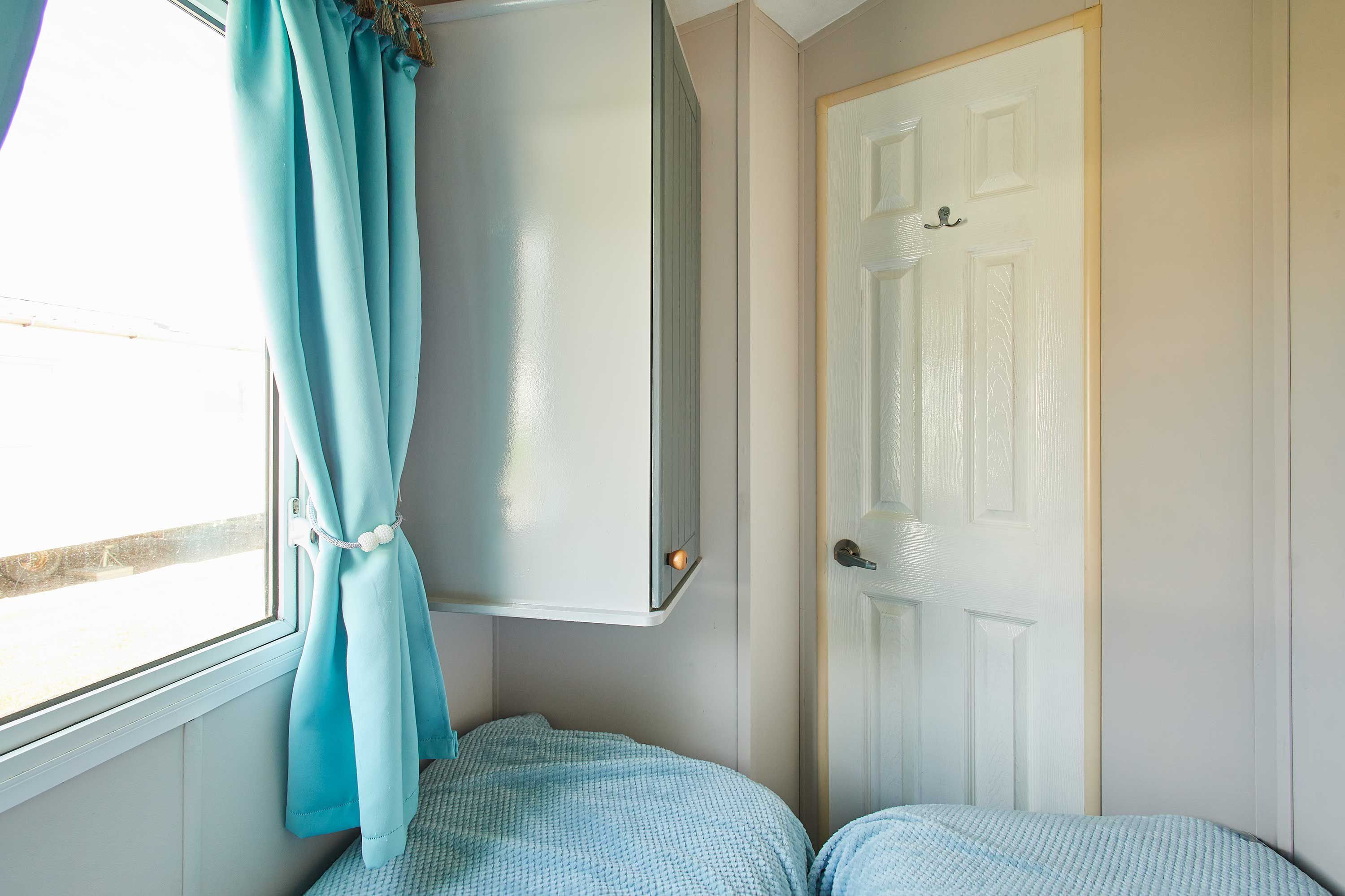 Ein Schlafzimmer mit Bett, Fenster mit Vorhängen, einer Tür und einem Kleiderschrank.