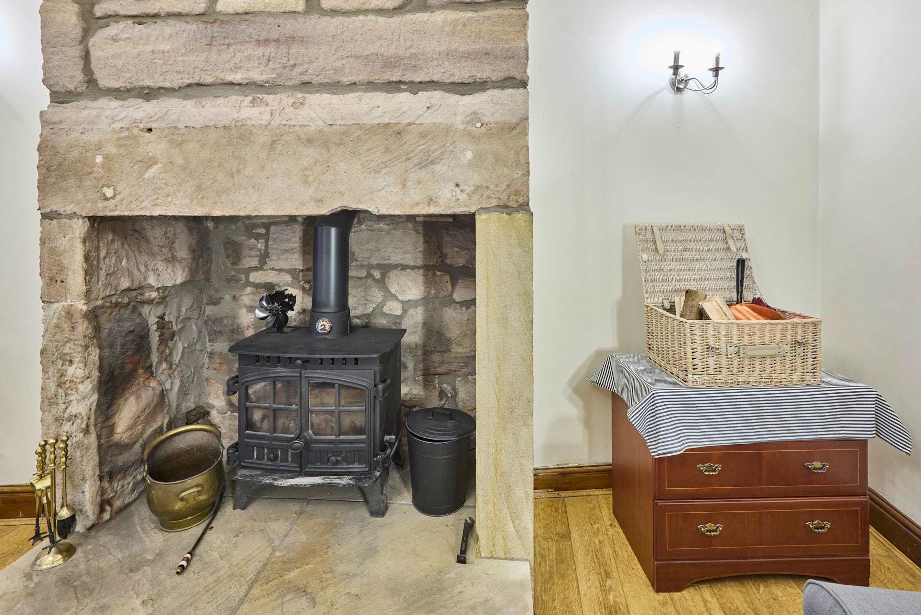 A stone fireplace with a black stove, a brass pot, and a black trash can.