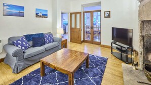A living room with a sofa, coffee table, TV, fireplace, and artwork on the walls. - Host Stay Puffin Cottage (Seahouses)