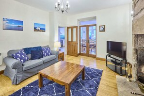 A living room with a sofa, coffee table, TV, fireplace, and artwork on the walls. - Host Stay Puffin Cottage (Seahouses)