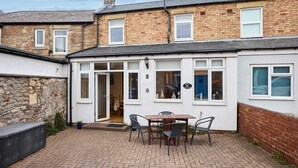 A brick house with a white exterior, a patio with a table and chairs, and a blue door. - Host Stay Puffin Cottage (Seahouses)