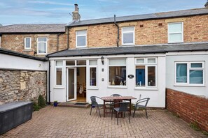 A brick house with a white exterior, a patio with a table and chairs, and a blue door. - Host Stay Puffin Cottage (Seahouses)