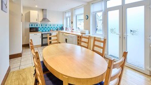 A modern kitchen with a dining area, large windows, and a view of the city. - Host Stay Puffin Cottage (Seahouses)
