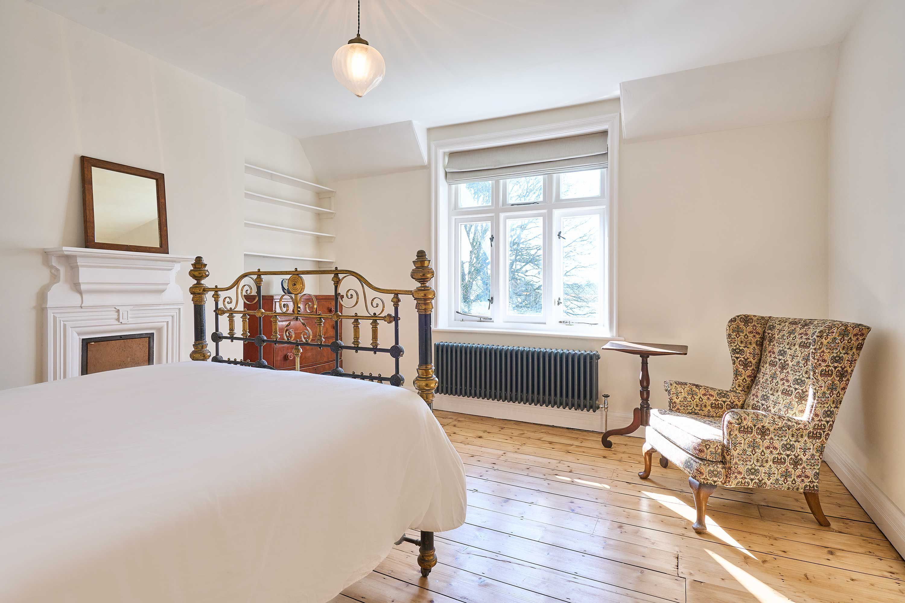 Quarto com cama grande, uma cadeira, lareira e janela com vista.