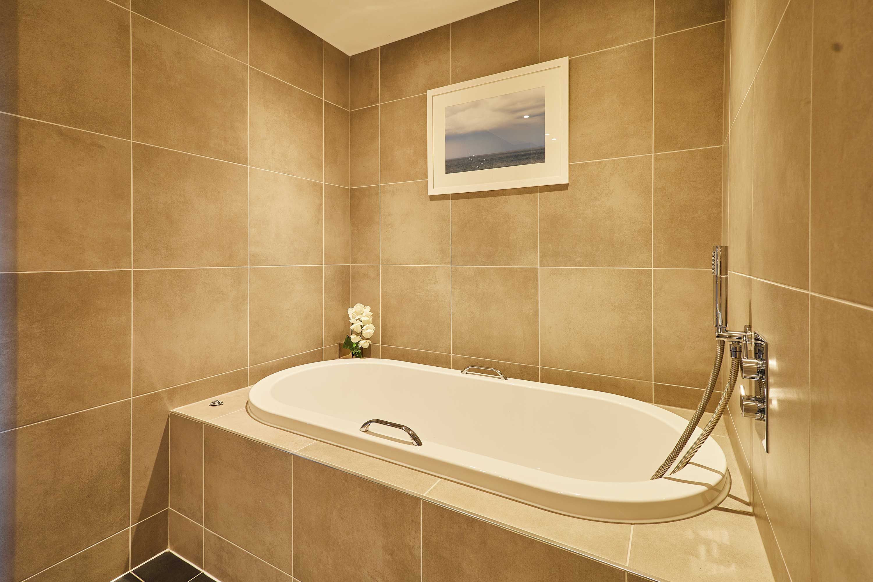 A bathroom with a bathtub, a framed picture on the wall, and a small vase with flowers.