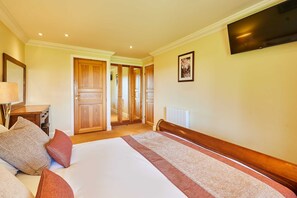 Habitación de hotel con una cama grande, armario de madera, mesita de noche, lámpara y televisor montado.