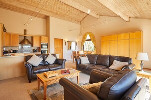 Amplia sala de estar con sofás de cuero, una mesa de centro de madera y una cocina al fondo.