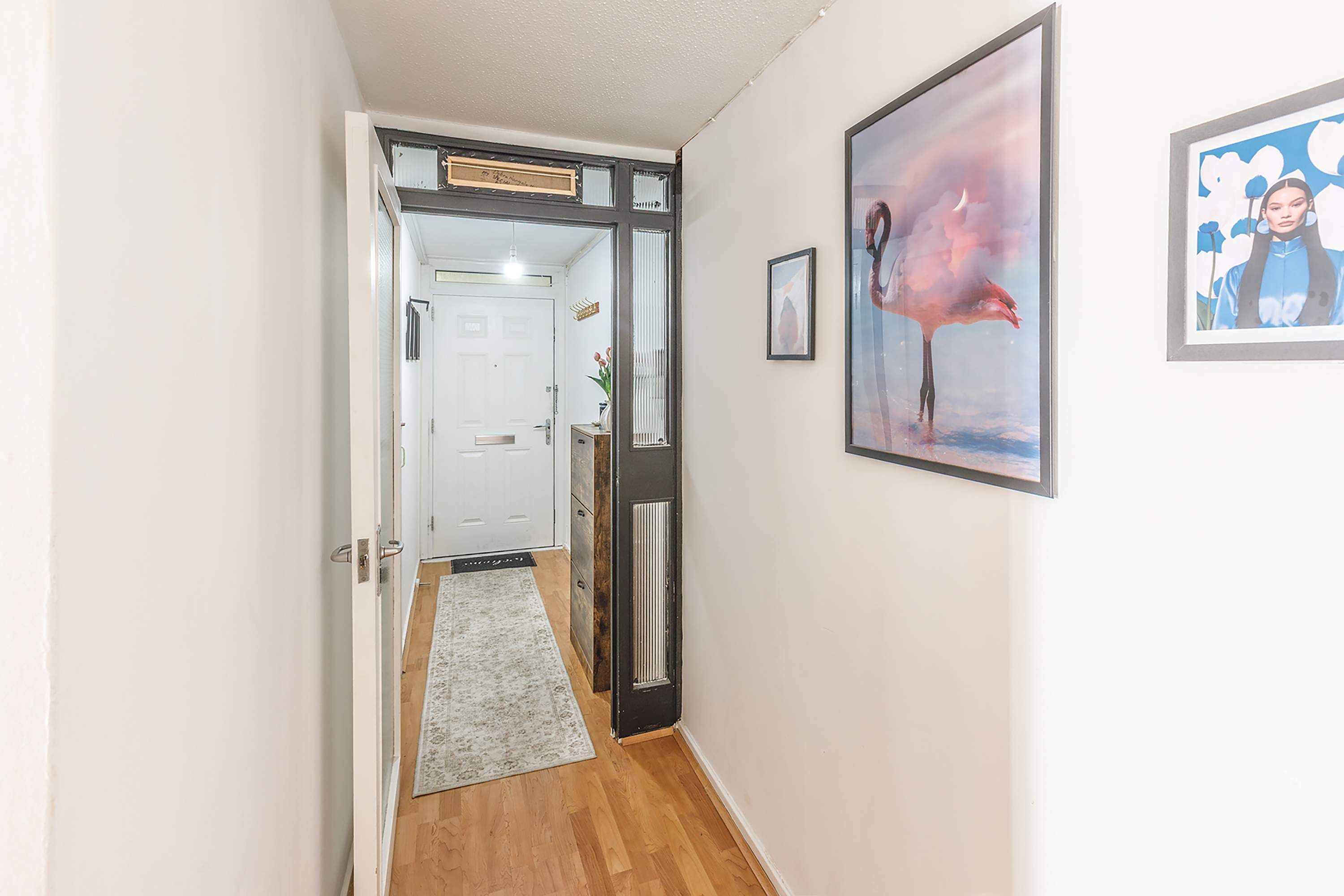 A hallway with a wooden floor, a white door, and a framed painting on the wall.