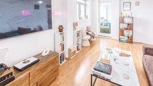 A modern living room with a large flat-screen TV, wooden furniture, a coffee table with books, and a bookshelf. - Host Stay Essex Place (Brighton)
