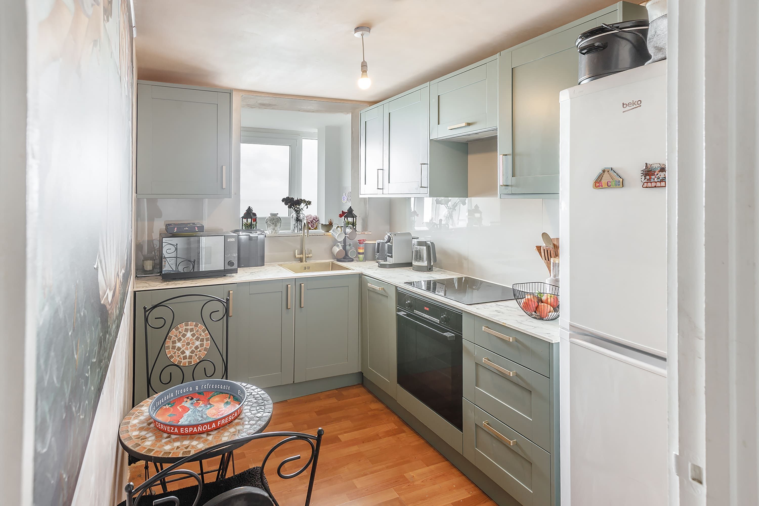 A kitchen with grey cabinets, a white refrigerator, a dining table with chairs, and a coffee machine.