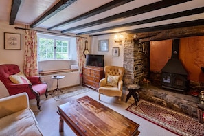 Une chambre de style traditionnel avec des poutres apparentes, une cheminée en pierre, un téléviseur et un fauteuil rouge.