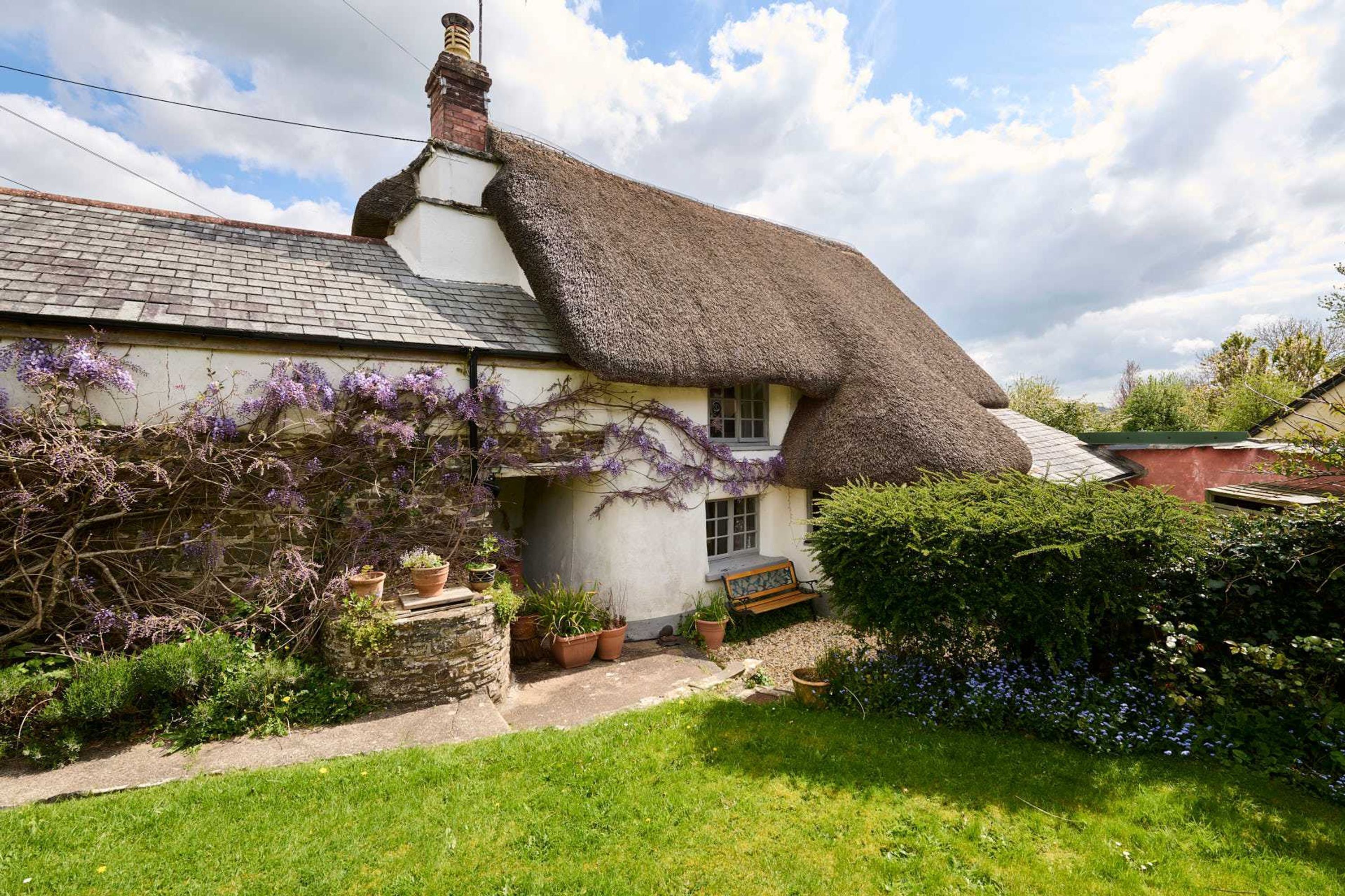 A traditional thatched-roof cottage with a stone foundation, a small porch, and potted plants.