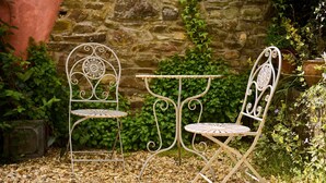A garden with a stone wall, two metal chairs, and a small table. - Host Stay Wistermead Cottage (Winkleigh)
